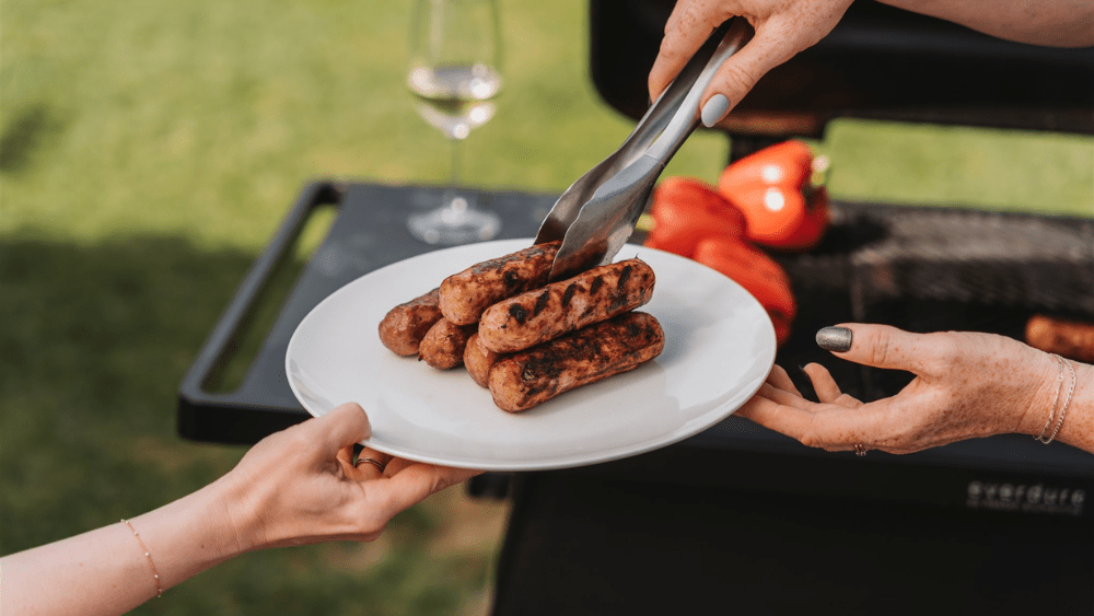 Plate of BBQ sausages being passed between two people.