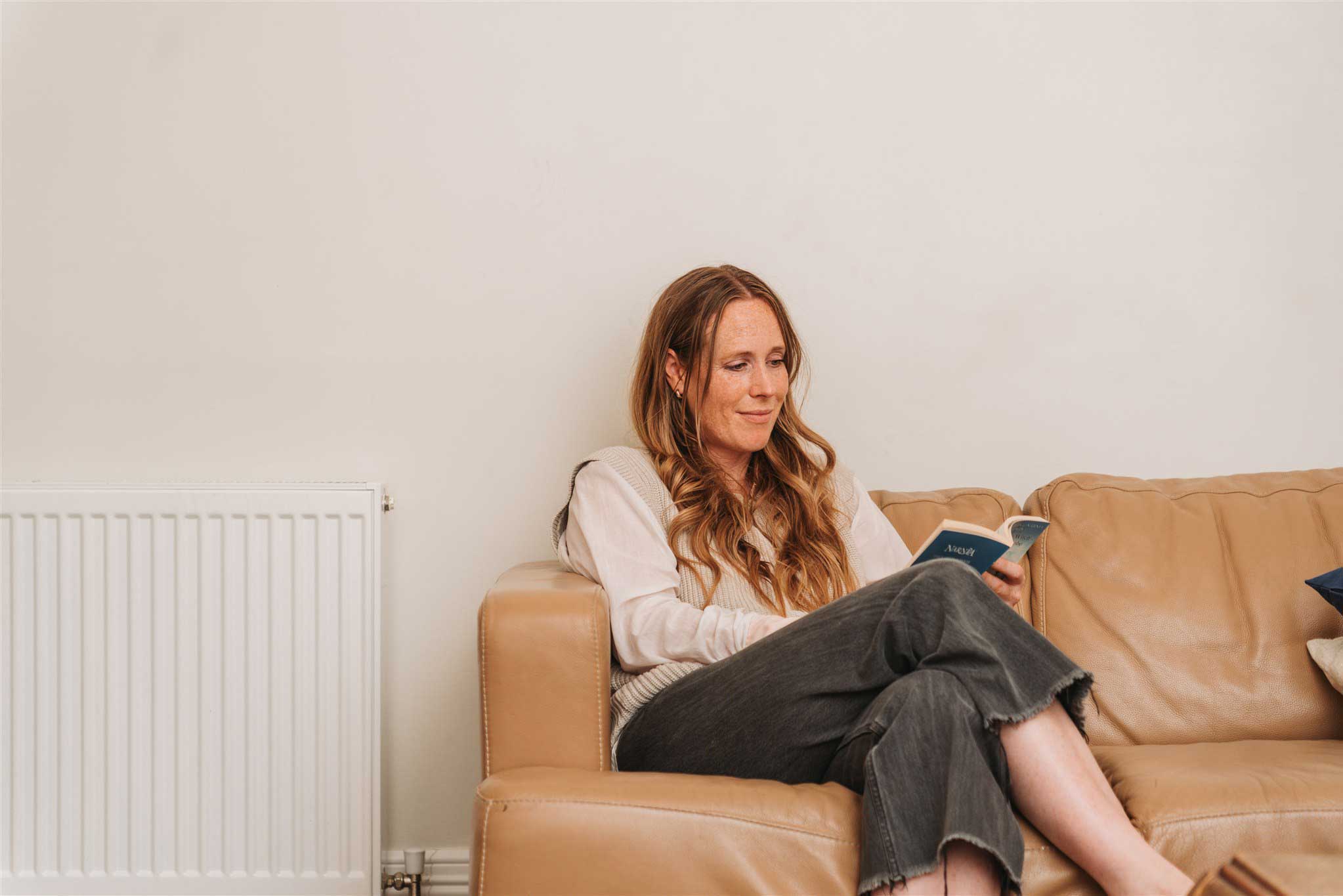 Woman sitting on couch reading a book by a gas radiator