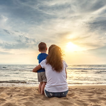 woman and child sitting on beach looking at sunset
